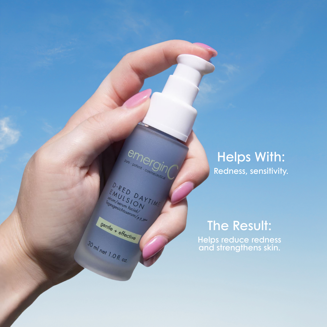 Hand holding a bottle of emerginC D-Red Daytime Emulsion against a blue sky background